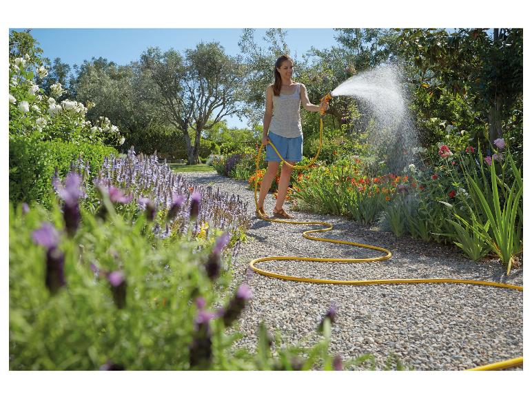 Frau bewässert einen Gartenweg mit gelbem Schlauch und Spritzpistole.