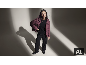 Eine Frau in einer lila Daunenjacke, einem schwarzen Pullover und einer schwarzen Hose posiert im Studio.