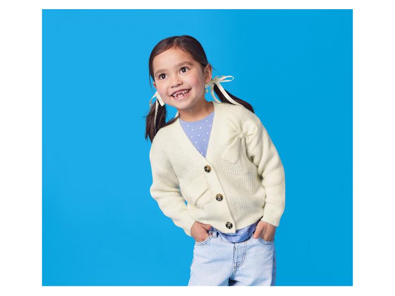 Glückliches Mädchen in cremefarbener Strickjacke, blauem T-Shirt und Jeans.