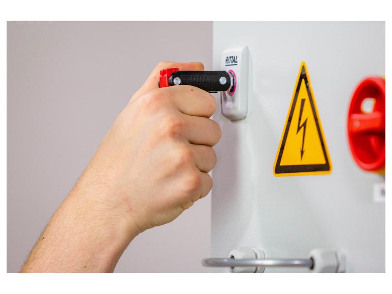 Hand benutzt Schlüssel zum Öffnen eines Elektroschaltschranks mit Warnzeichen.