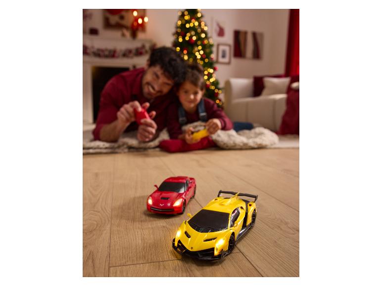 Vater und Sohn spielen mit ferngesteuerten Autos auf einem Holzboden, neben einem Weihnachtsbaum.