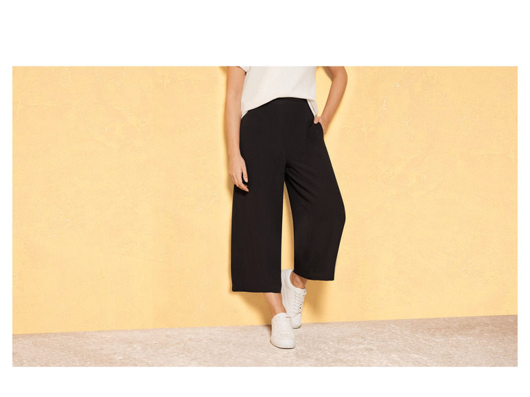 Eine Frau trägt eine schwarze, weite Hose und weiße Sneakers.