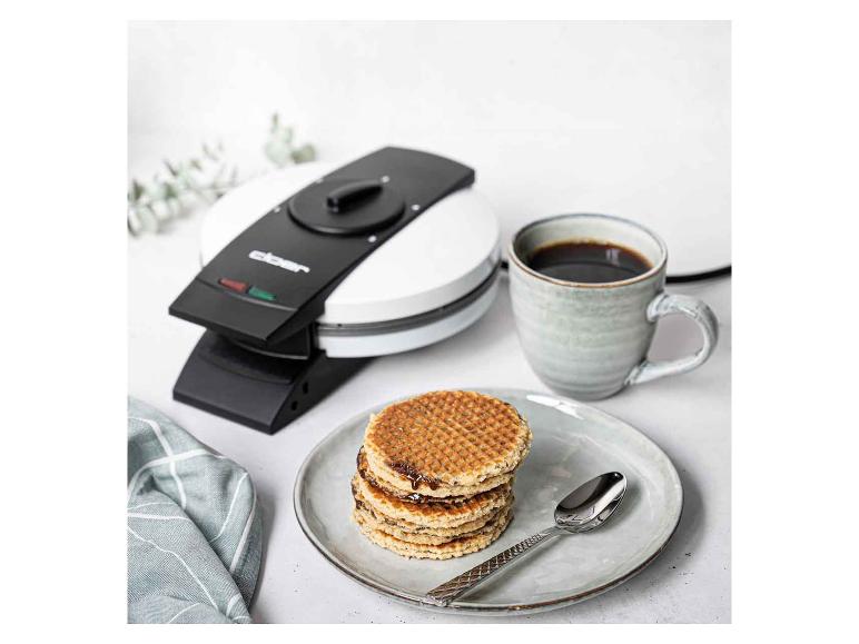 Waffeln mit Schokolade, Kaffee und Waffeleisen auf einem weißen Tisch.