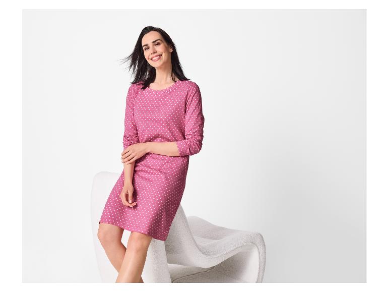 Frau in einem rosa gepunkteten Kleid sitzt auf einem weißen Stuhl und lächelt.