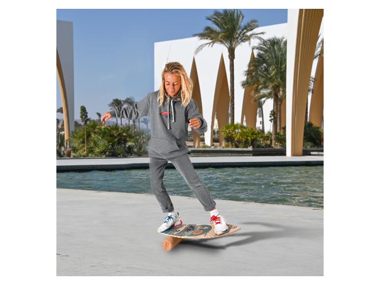 Junge in grauem Trainingsanzug balanciert auf einem Balance Board im Freien.