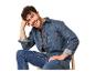 Lächelnder Mann in Jeanshemd und Jeans, auf einem Stuhl sitzend.