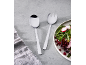 Silbernes Salatbesteck auf grauem Hintergrund neben einem Salat mit Granatapfel und Radieschen.
