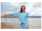 Frau in hellblauem Hemd und Hose am Strand mit einer Stadt im Hintergrund