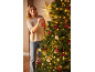 Frau schmückt einen Weihnachtsbaum mit roten und goldenen Kugeln und warmen Lichtern.