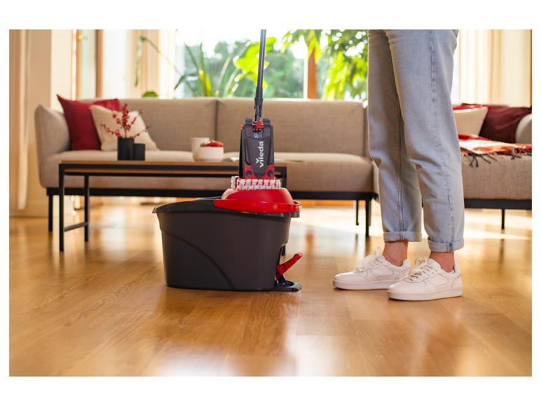 Person reinigt einen Holzboden im Wohnzimmer mit einem Vileda Mopp und Eimer.
