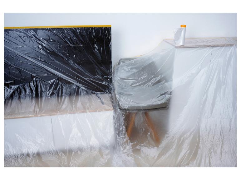 Ein Fernseher, ein Stuhl und ein Schrank, die mit Plastikfolie für Malerarbeiten abgedeckt sind.