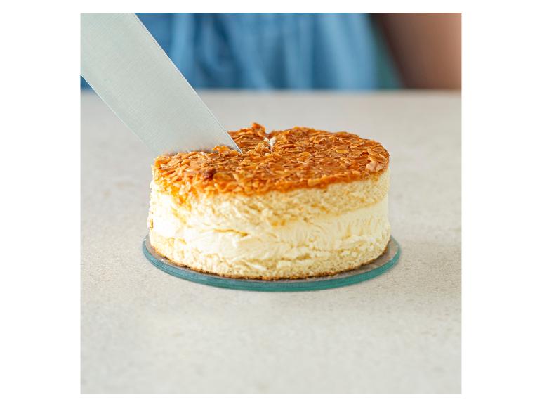 Ein Messer schneidet einen Kuchen mit Sahne und Mandeln.