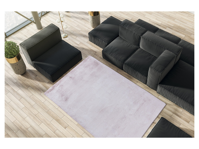 Ein rosafarbenes Teppich auf einem Holzboden mit einer schwarzen modularen Couch.