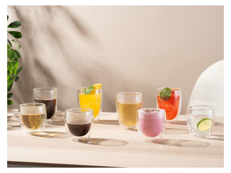 Verschiedene Getränke in doppelwandigen Gläsern auf einem Holztisch mit natürlichem Licht.