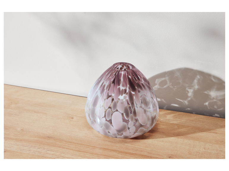 Eine Glasvase mit rosa und grauen Punkten auf einem Holztisch.