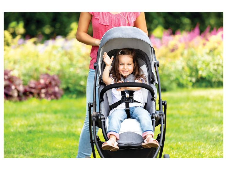 Ein Kind in einem grauen Kinderwagen in einem grünen Garten.