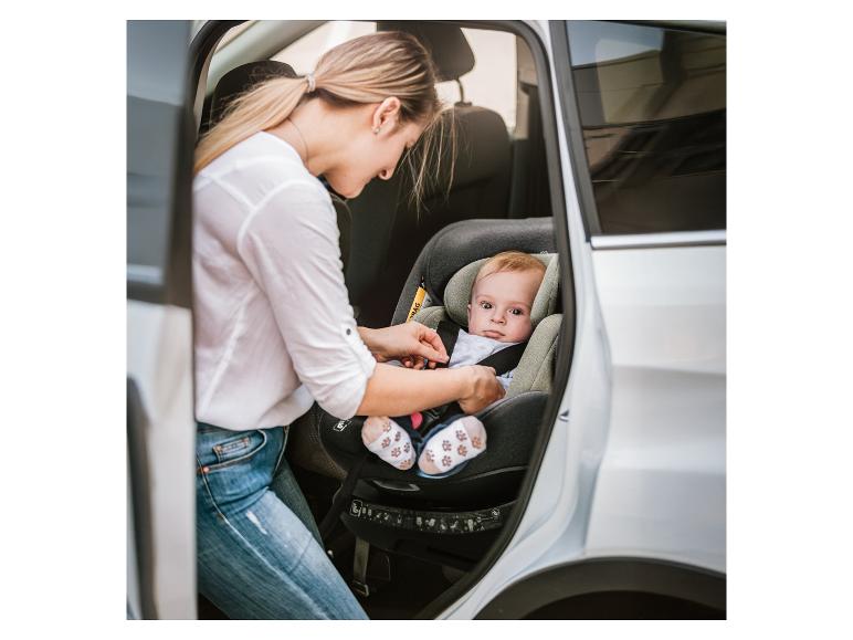 Frau schnallt Baby im Kindersitz im Auto an.