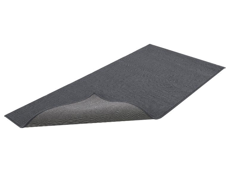 Dunkelgraue Badematte oder Teppich mit hochgeklappter Kante, die die rutschfeste Unterseite zeigt.
