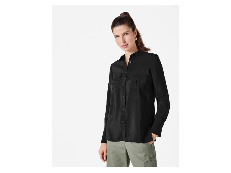 Eine Frau trägt eine schwarze Bluse mit langen Ärmeln und eine grüne Hose.