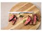 Steakmesser und geschnittenes Steak mit Kräutern und Gewürzen auf einem Holzbrett.
