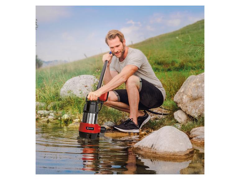 Mann benutzt eine Wasserpumpe in einem Bach, umgeben von Natur.