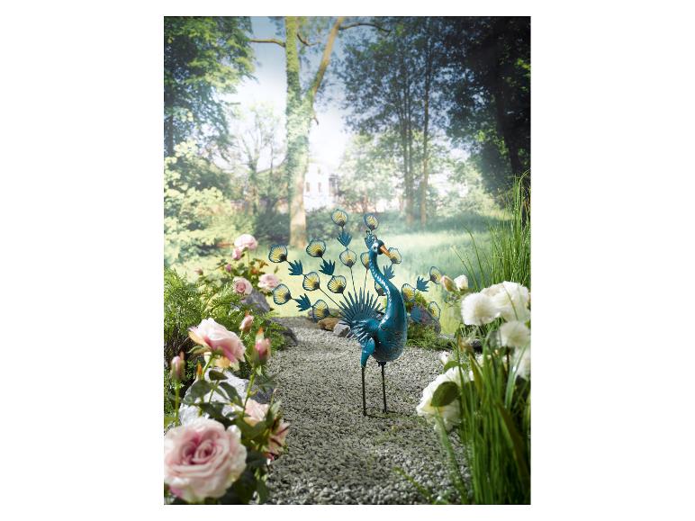 Metall-Pfau-Skulptur, Rosen und Grünpflanzen im Garten.