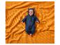 Baby in dunkelblauem Bärenanzug auf einer orangefarbenen Waffeldecke.