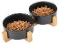 Zwei schwarze Tierfutternäpfe, gefüllt mit Trockenfutter, auf Holzständern.