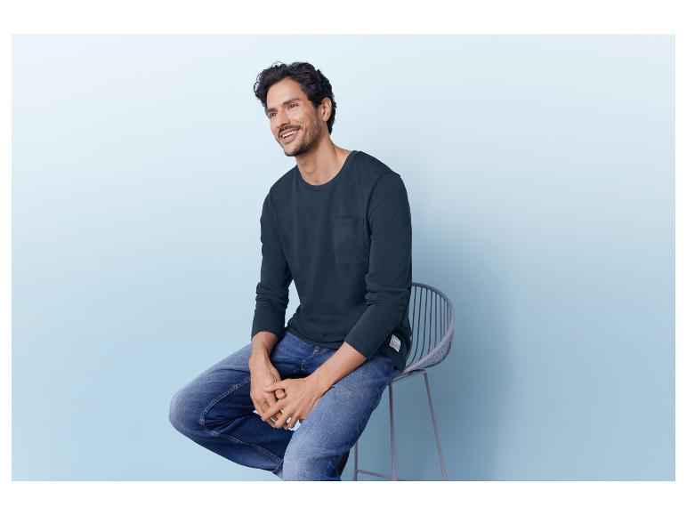 Mann in einem dunkelblauen Langarmshirt und blauen Jeans.