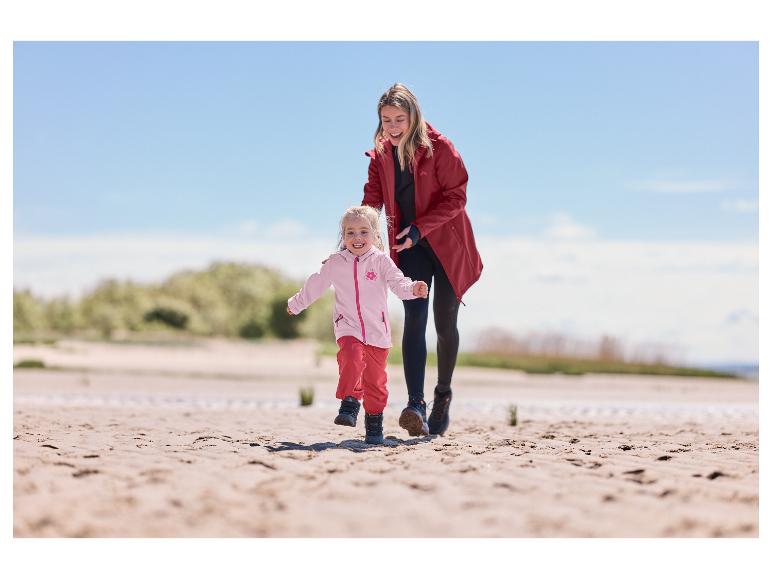 Mutter und Kind in wasserdichten Jacken und Hosen am Strand.