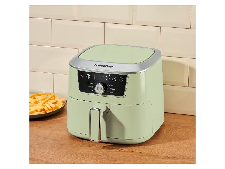 Hellgrüne Heißluftfritteuse mit Digitalanzeige (175 Grad) auf einer Holztheke neben einem Teller Pommes.