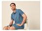Mann in blauem Poloshirt und Shorts sitzt auf einem Stuhl.