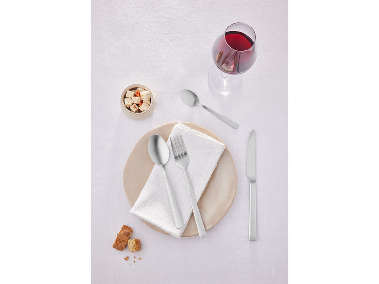 Ein gedeckter Tisch mit Besteck, Teller, Weinglas und Snack.