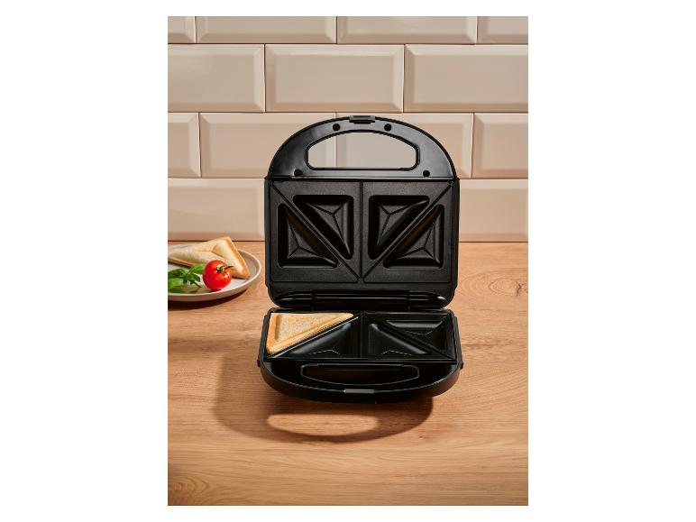Offener Sandwichmaker mit einem getoasteten Sandwich darin, auf einer Holztheke.