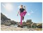 Frau in schwarzem T-Shirt und fuchsiafarbenen Leggings trainiert am Felsenstrand.