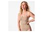 Frau in beigem Shapewear-Top und Slip, Hand an der Hüfte, blickt in die Kamera.