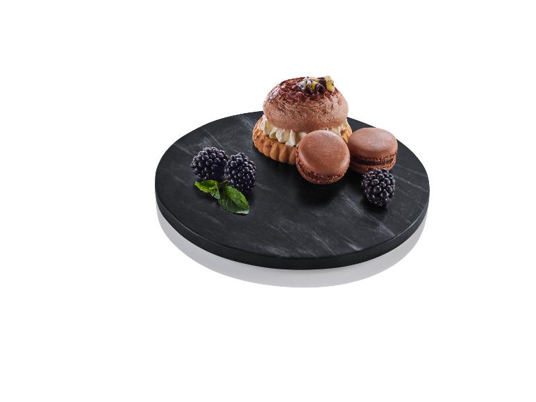 Schokoladen-Macarons und ein Gebäck mit Sahne auf einem schwarzen Marmorteller.