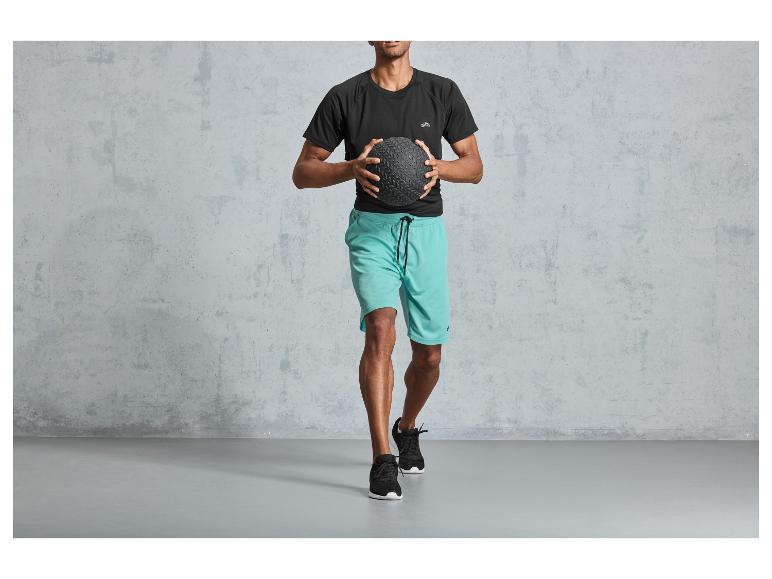 Mann in schwarzem T-Shirt und blauen Shorts hält einen Medizinball.