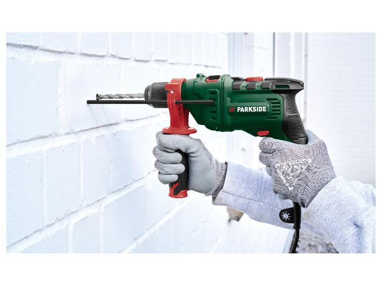 Mann in Schutzhandschuhen bohrt mit einem Schlagbohrer in eine weiße Wand.