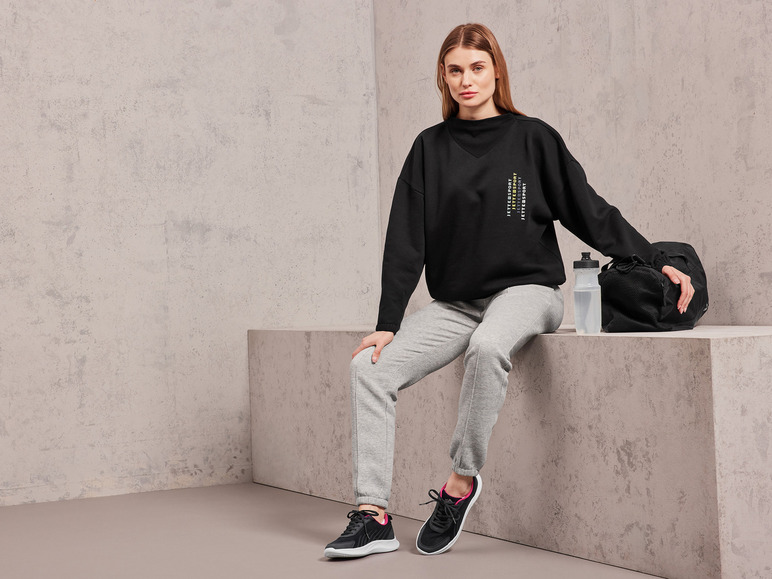 Eine Frau trägt einen schwarzen Jette Joop Pullover, graue Jogginghose und schwarze Sneaker.