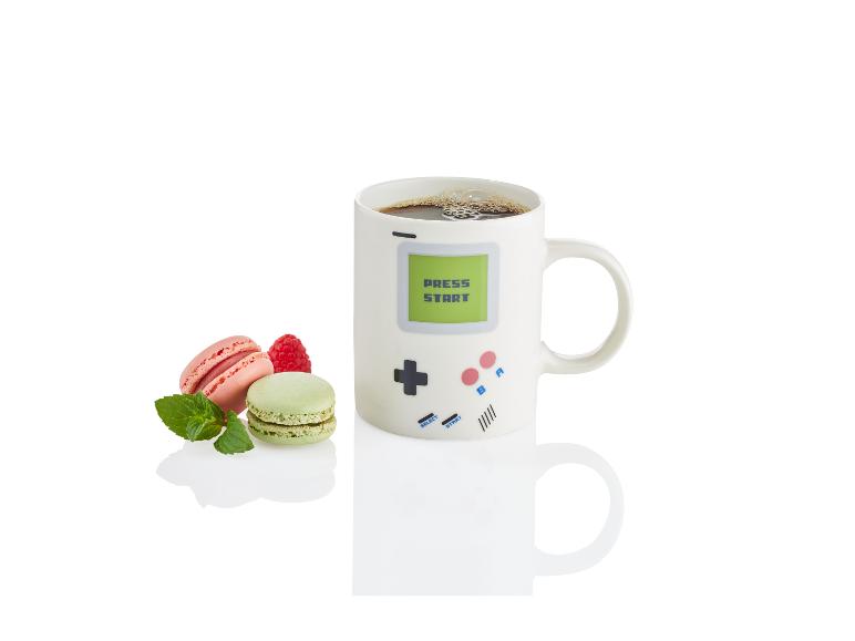 Eine Tasse mit Retro-Spieldesign, gefüllt mit Kaffee und Macarons.
