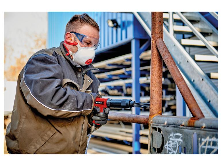 Mann entfernt mit einem pneumatischen Nadelentroster Rost von einem Metallrohr.