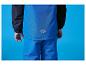 Kind in blauer und schwarzer Skijacke und Skihose mit Berglogo auf dem Rücken.