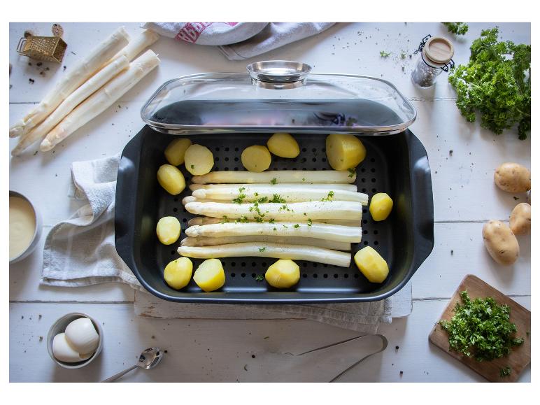 Weißer Spargel und Kartoffeln in einer Auflaufform mit Glasdeckel, umgeben von frischen Zutaten.