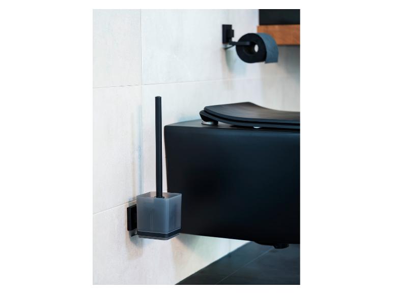 Eine schwarze Toilettenbürste und ihr Halter sind an einer weiß gefliesten Wand neben einer schwarzen Toilette und einem Toilettenpapierhalter angebracht.