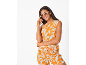 Lächelnde Frau in orangefarbenem Top und Shorts mit weißem Blumenmuster, Sonnenbrille und Creolen.