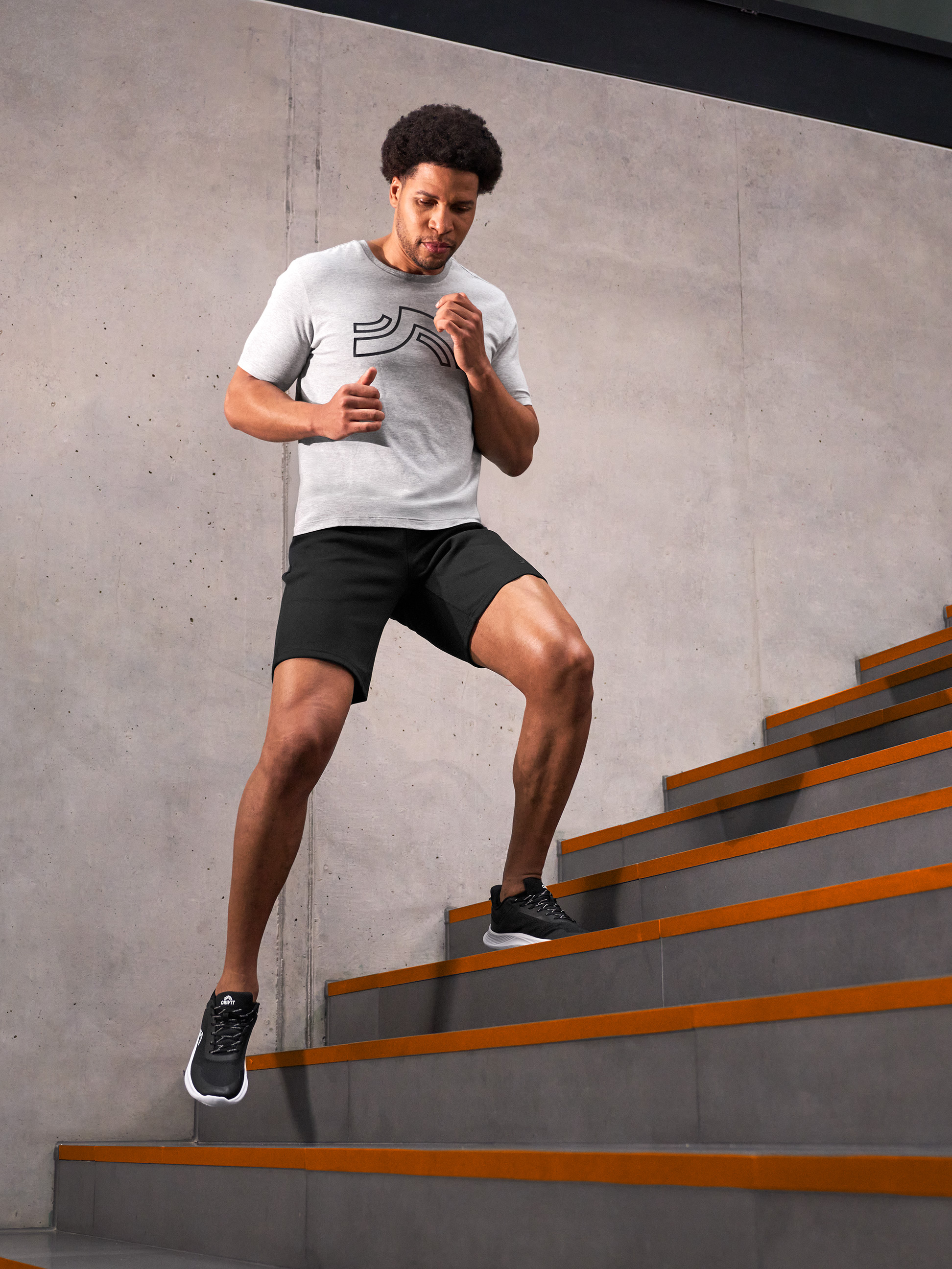 Mann in grauem T-Shirt und schwarzen Shorts läuft Betontreppen mit orangefarbenen Streifen hoch.