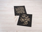 Zwei schwarze Karten mit goldenen Blumenmotiven und zwei Holzstiften.