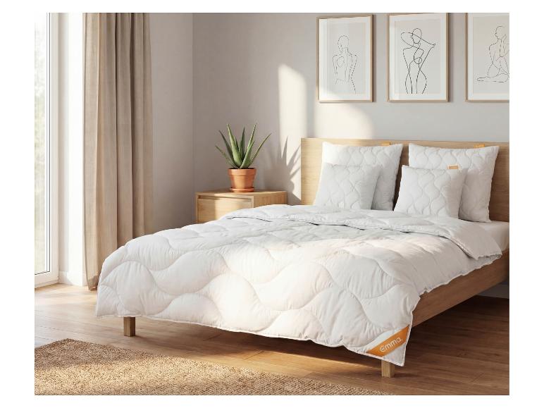 Schlafzimmer mit Bett, weißer gesteppter Bettwäsche, Kissen und Holzkopfteil.