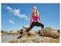 Frau in fuchsiafarbenem Sporttop und schwarzen Capri-Leggings dehnt sich auf Felsen am Strand.
